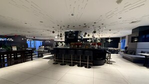 A modern bar area with a central bar, multiple seating options, and a ceiling with unique lighting fixtures. - Acqua Novotel Suites w/ Rockwell View (Mandaluyong City)