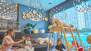 Ein modernes Wohnzimmer mit großem Fenster, einer Couch, einer Holzlade und einem Kind, das mit Bauklötzen spielt.