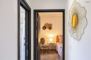 A hallway with a door leading to a room with a bed, a chair, a nightstand, and wall art. - Air-conditioned Casa di Castagni near Saint Florent (OLETTA)