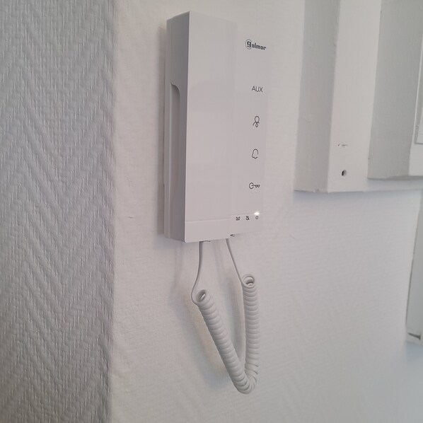 A white wall-mounted telephone with a coiled cord, a key symbol, and a power button. - Beautiful Brest Kérinou apartment refurbished (Brest)