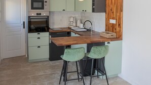 Uma cozinha moderna com armários verdes, bancada de madeira e dois bancos altos.