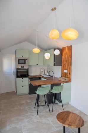 A modern kitchen with green cabinets, a wooden countertop, and two bar stools. - Fully renovated mazet en provence (Saint-Étienne-du-Grès)