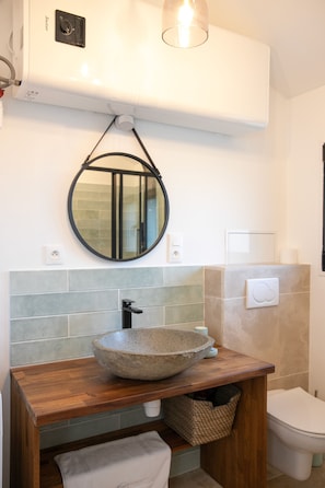A bathroom with a wooden vanity, a round mirror, a stone sink, and a toilet. - Fully renovated mazet en provence (Saint-Étienne-du-Grès)