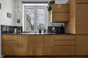 A modern kitchen with wooden cabinets, a marble countertop, and a view of trees through a large window. - Muranów Apt - Metro, Top Location - by Rentujemy (Warszawa)