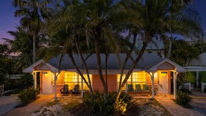 A beachfront house with a covered porch, palm trees, and a sandy driveway.