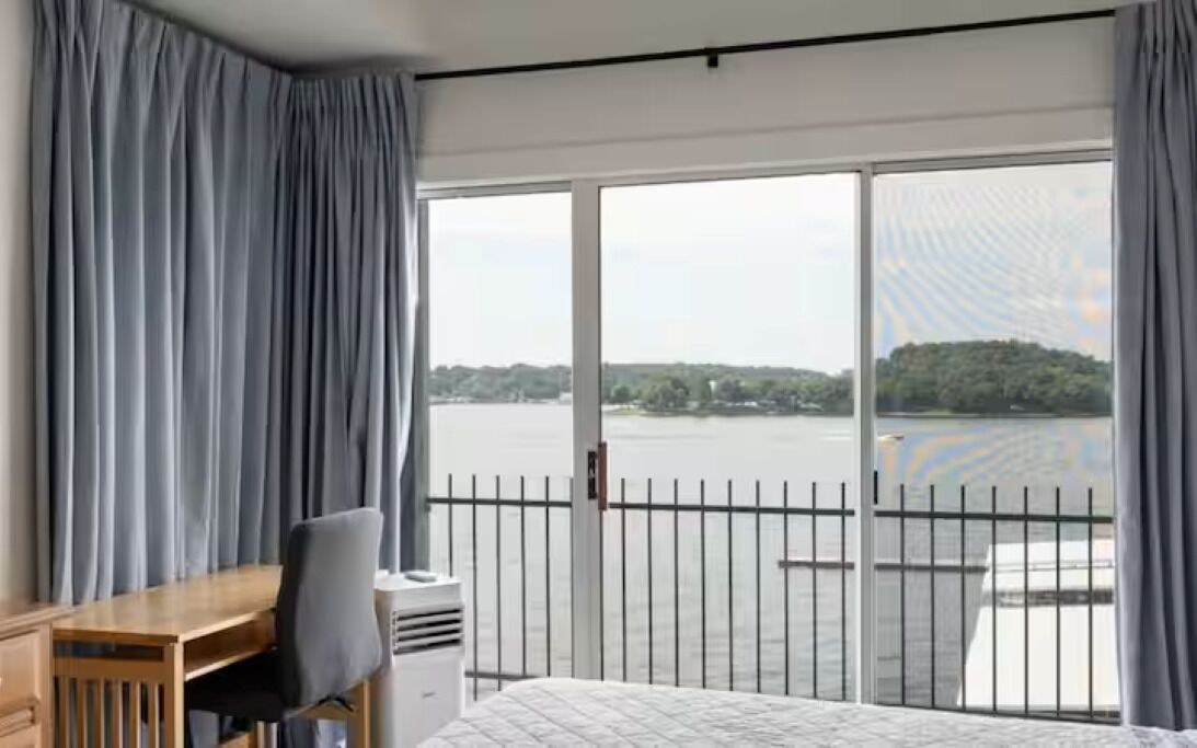 A hotel room with a large window, a bed, a desk, and a chair.