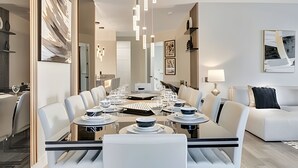 A modern dining area with a long table, white chairs, and hanging pendant lights. - Vista Cay 4BR Luxury Near Universal Studios (Orlando)