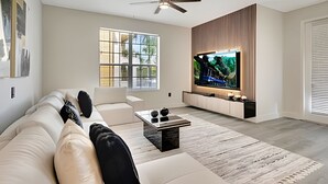 A modern living room with a large flat-screen TV, a ceiling fan, and a large window providing natural light. - Vista Cay 4BR Luxury Near Universal Studios (Orlando)