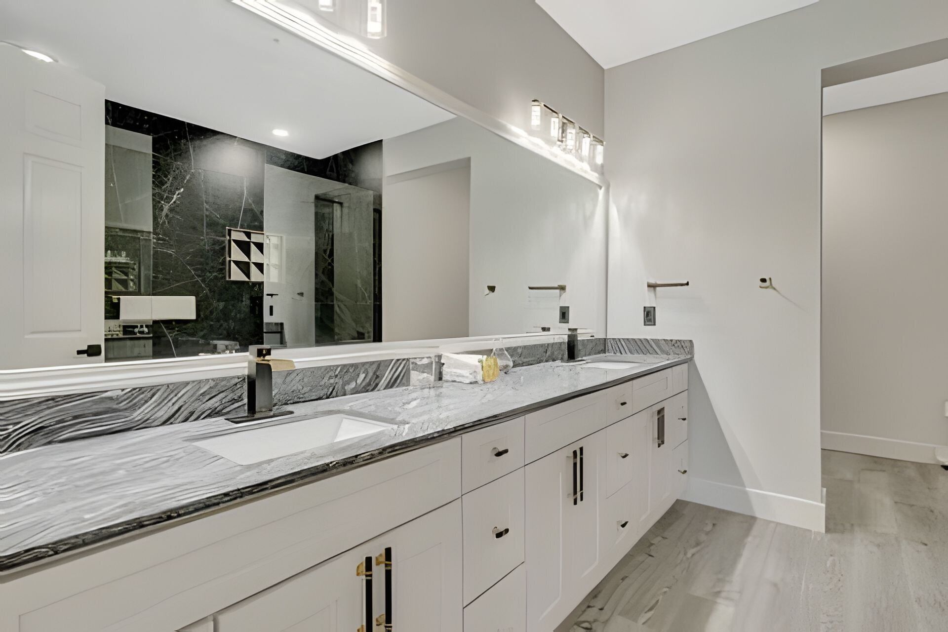 A modern bathroom with a large mirror, two sinks, and a marble countertop.