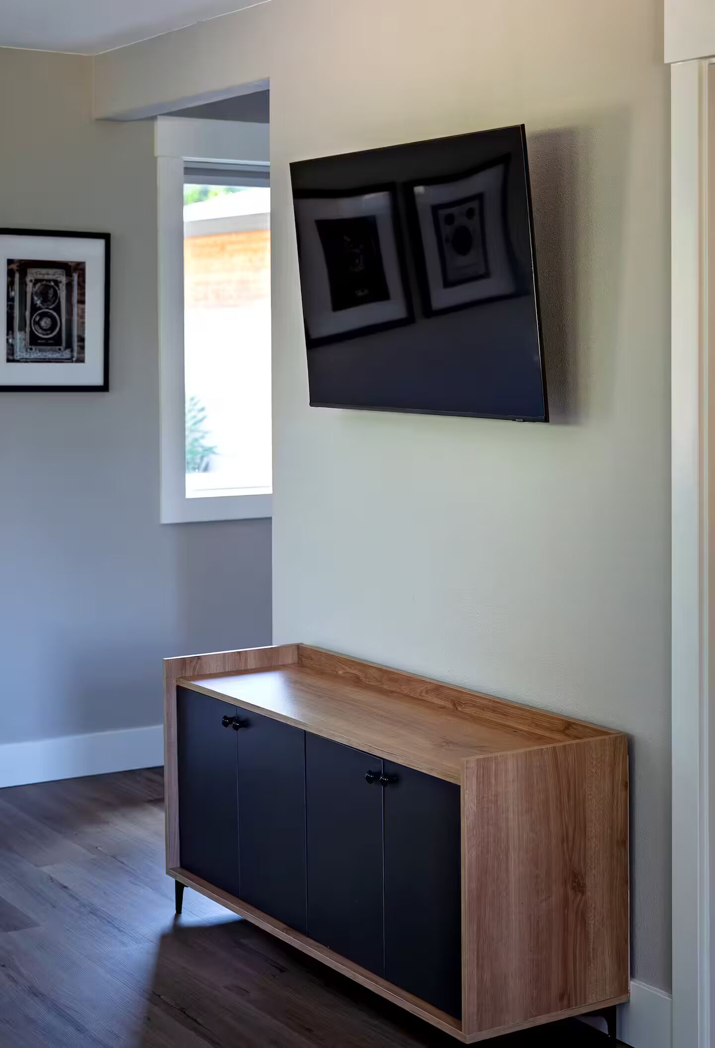 A modern room with a wooden cabinet, a flat-screen TV mounted on the wall, and a framed picture.