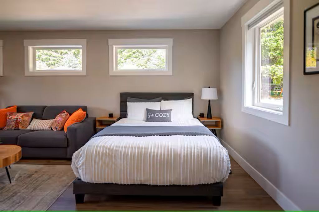 A bedroom with a bed, a sofa, and two windows.