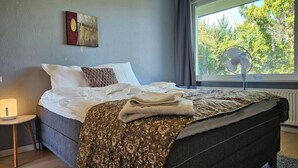 Een net opgemaakt bed met een deken met patroon, een bedlampje en een kunstwerk aan de muur.