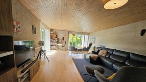 Een moderne woonkamer met een houten plafond, een leren bank, een televisie en een boekenkast.