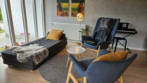 Een moderne woonkamer met een bank, een fauteuil, een bijzettafeltje en een piano.