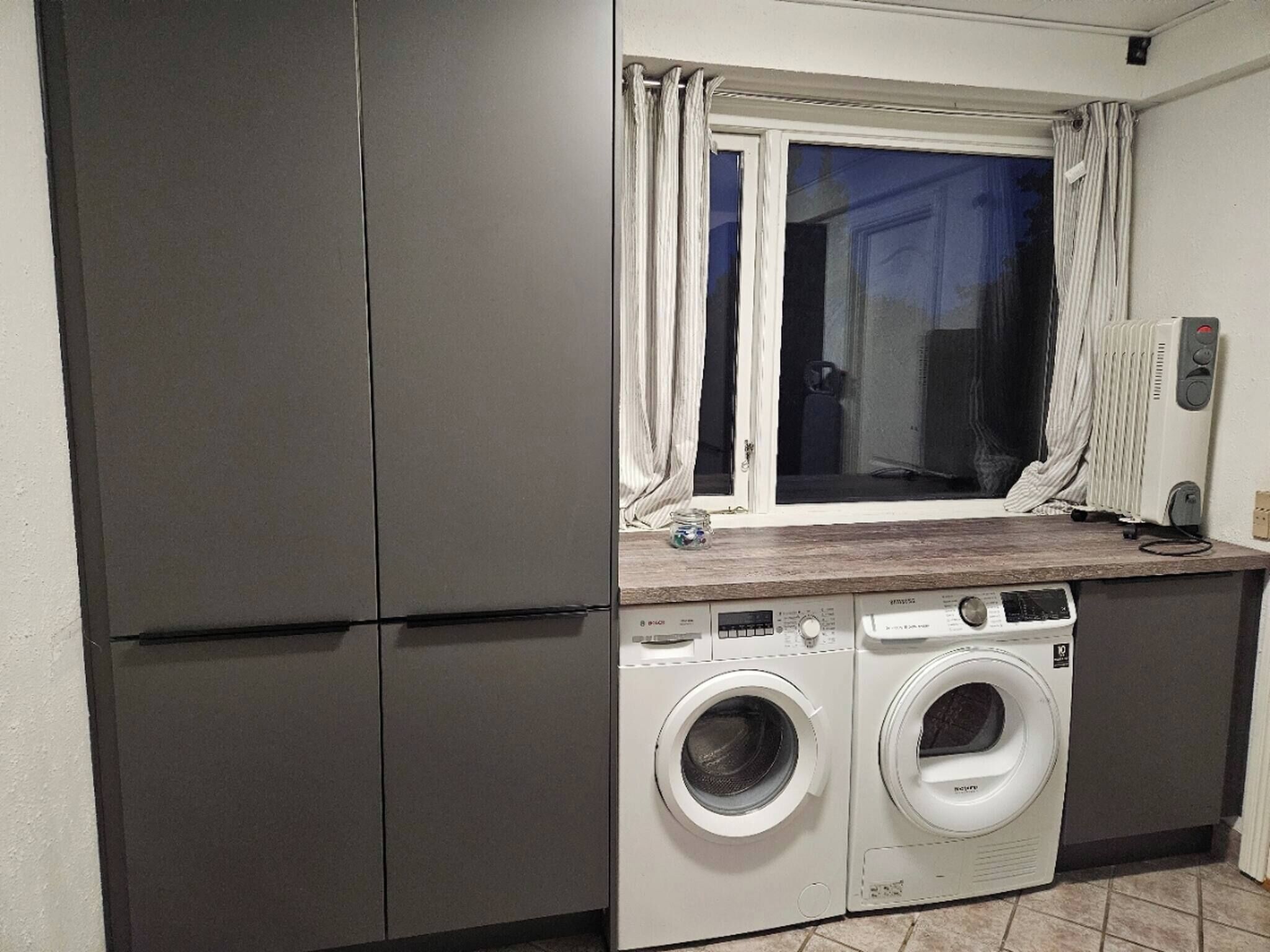 A compact kitchen with a built-in washer and dryer, a window with curtains, and a radiator.