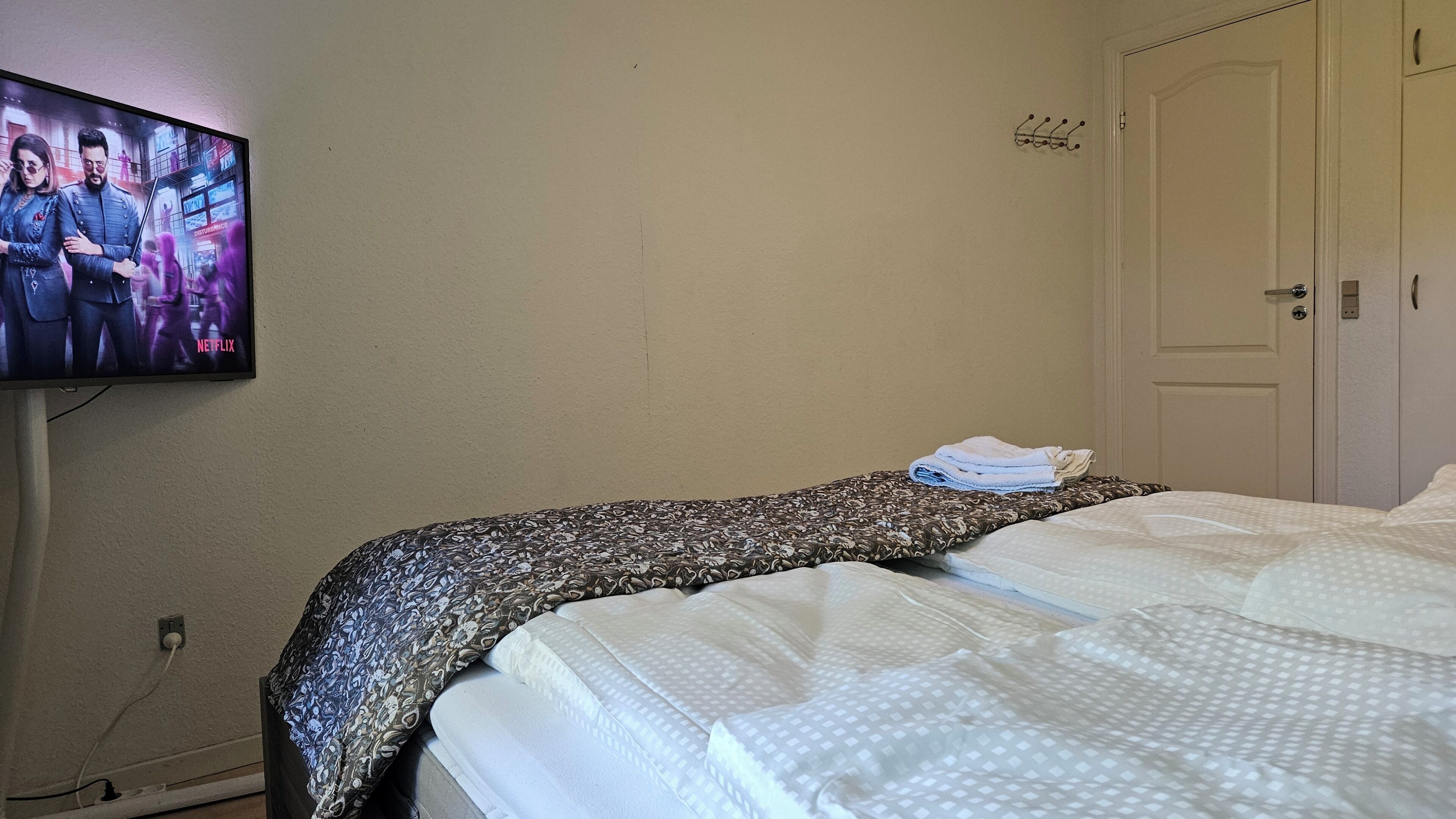 A hotel room with a bed, a television mounted on the wall, a door, and a coat rack.