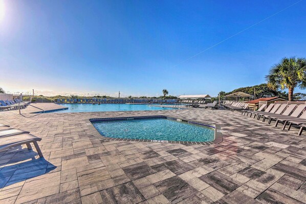 Un espace piscine doté d’un sol carrelé, de chaises longues et d’un palmier.