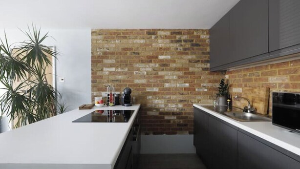 Eine moderne Küche mit Ziegelwand, einer zentralen Kochinsel, dunklen Schränken und einem eingebauten Backofen.
