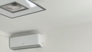 A room with a mounted air conditioner, a flat-screen TV, a door leading to another room, and a wall-mounted power outlet with a cable. - Apartment Sky Garden Rapallo Maria Jose Liguria-Attico sea view-Idro-Box (rapallo)