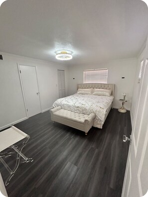 A bedroom with a bed, a bedside table, a chair, a window with blinds, and a door. - St Pete Family Beach House 10 mins from Madeira Beach, Game Room & Fire pit! (St. Petersburg)
