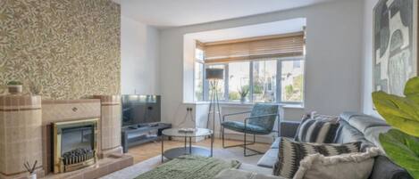 A modern living room with a fireplace, a sofa, a TV, and a window with blinds.