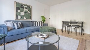 Una sala de estar con un sofá azul, una mesa de centro de vidrio y un comedor con una mesa y sillas.