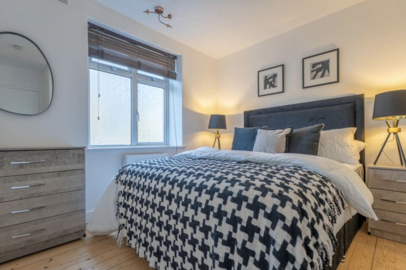 Ein Schlafzimmer mit einem Bett, zwei Nachttischen, einer Kommode, einem Fenster mit Jalousien und zwei gerahmten Bildern an der Wand.