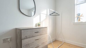 Una habitación con un aparador de madera, un espejo, una lámpara de pie y un ventanal con vista al cielo.