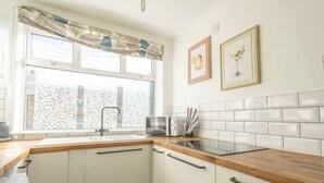 Una cocina con gabinetes blancos, encimera de madera, microondas y ventana con cortinas estampadas.