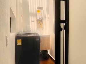 A compact room with a black washing machine, a small bucket, and a white radiator. - 2-bedroom Apartment with AC in Belén Aliadas (Medellín)