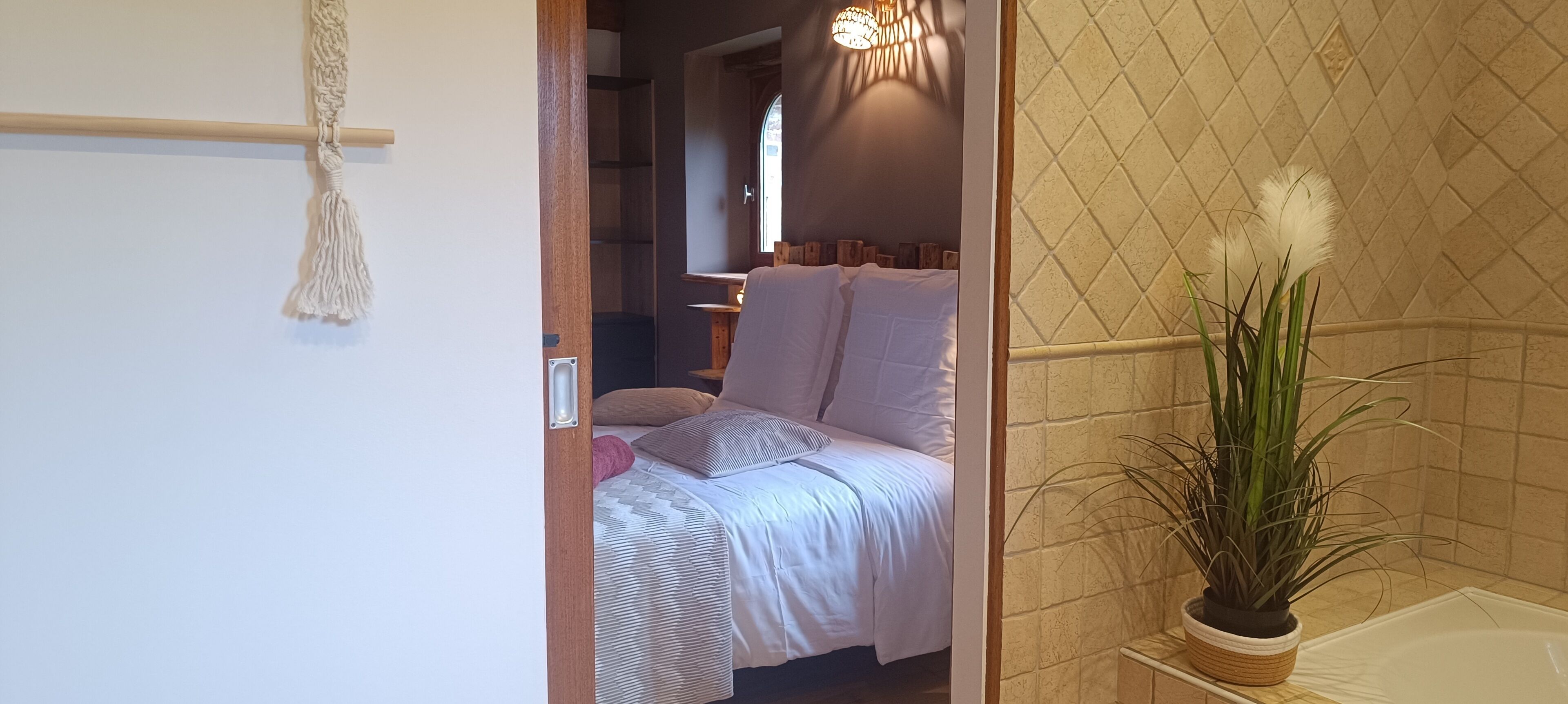 A bedroom with a bed, a bedside table, a potted plant, and a bathroom with a bathtub.