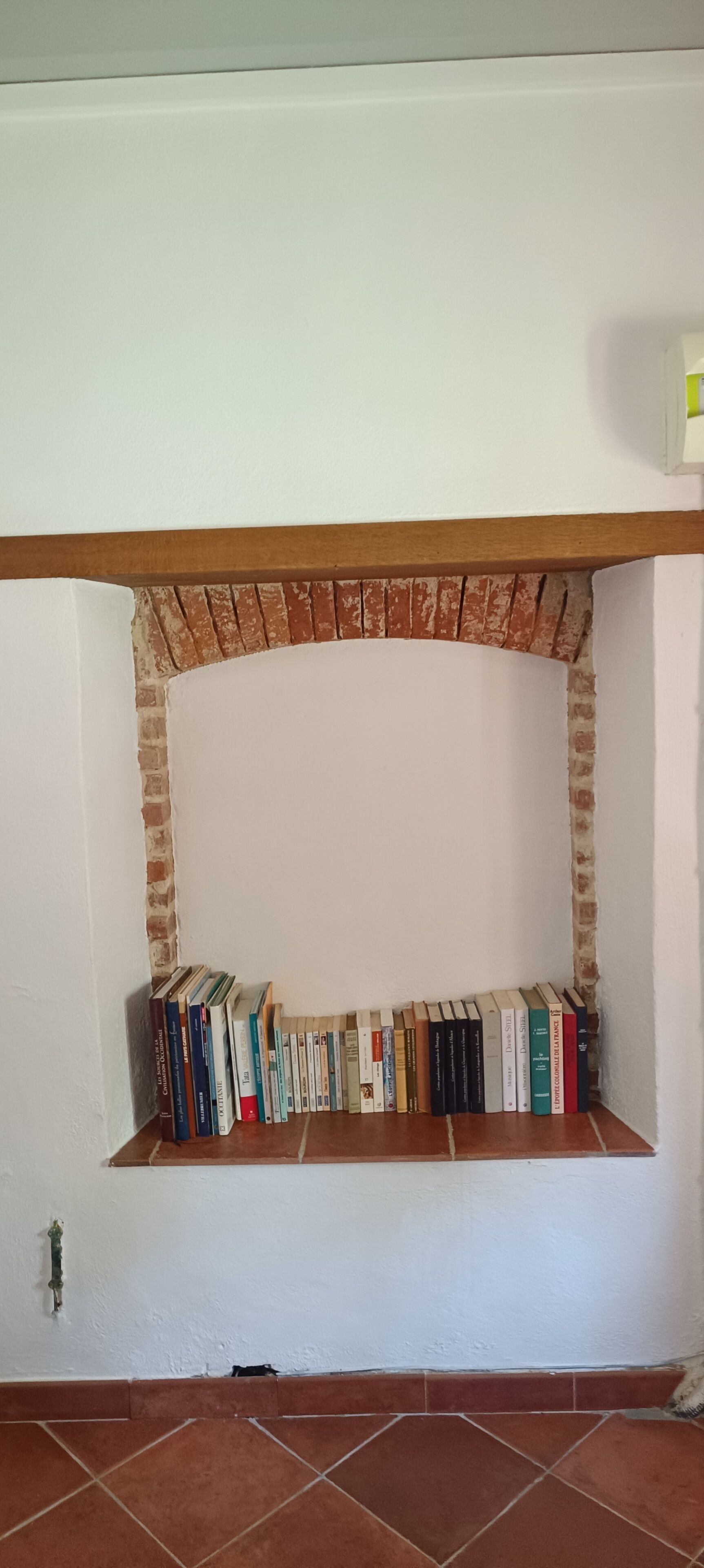 Ein Zimmer mit Kamin aus Backsteinen, einer weißen Wand und einem gefliesten Boden.