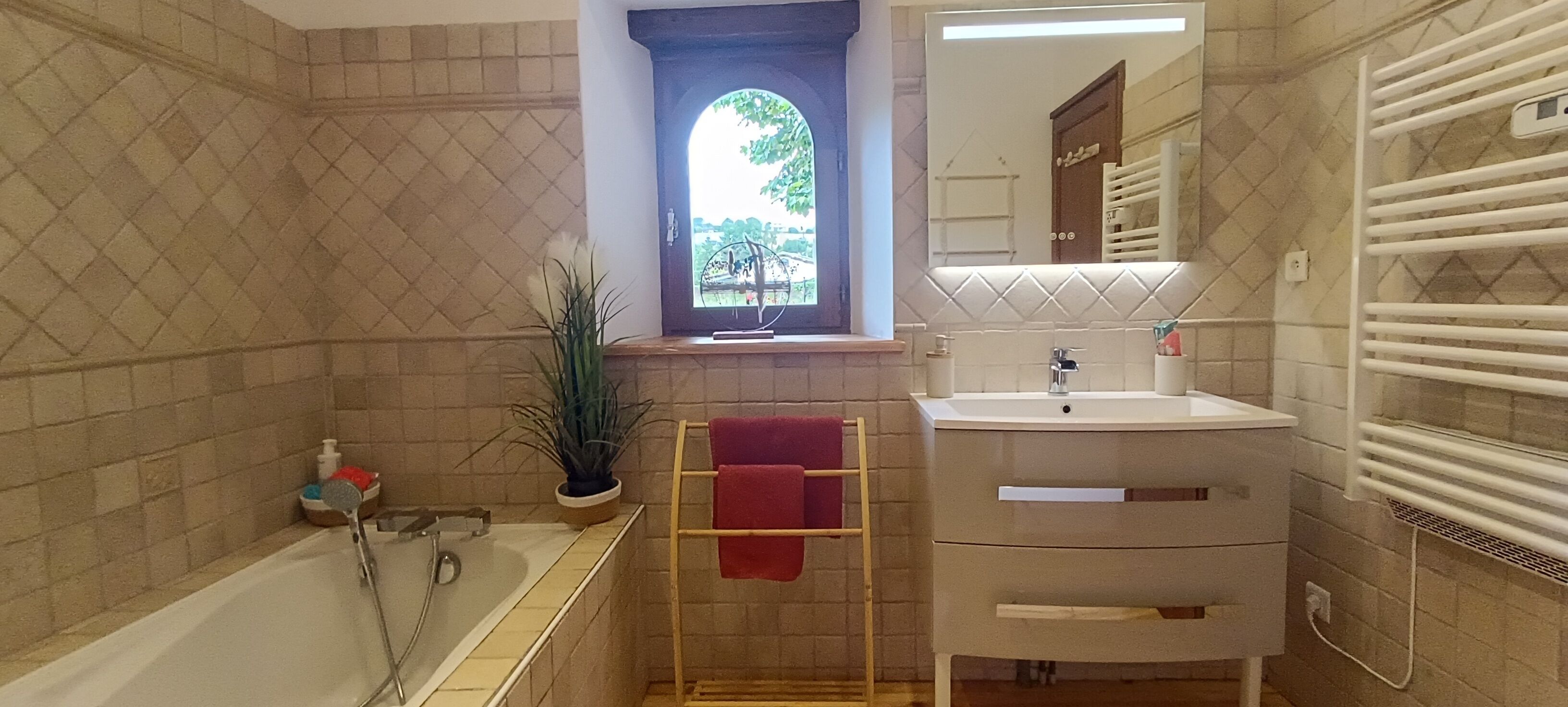 Un baño con bañera, lavamanos, espejo, ventana con vistas y toallero.