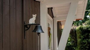 Un gato blanco sobre una repisa metálica negra fijada a una pared de madera, con una campana negra colgando debajo.