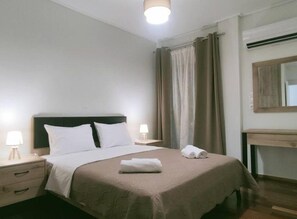 Una cama bien tendida con cabecera, dos mesitas de noche con lámparas, un escritorio de madera y un espejo en la pared.