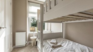 Une chambre avec un lit superposé, une fenêtre, un radiateur et une petite table de chevet.