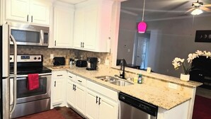 Una cocina moderna con armarios blancos, electrodomésticos de acero inoxidable, una encimera de granito y lavavajillas.