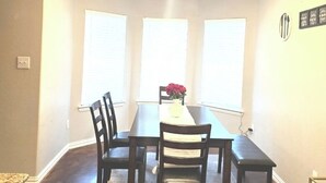 Un comedor con una mesa rectangular, cuatro sillas, un florero con flores y una lámpara en el techo.