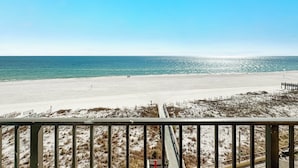 Strandudsigt fra en balkon med gelænder, sandstrand og hav.