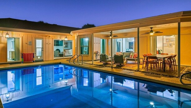 Ein Pool mit Glasveranda, ein Essbereich mit Tisch und Stühlen sowie ein Wohnzimmer mit Sofa und Fernseher.