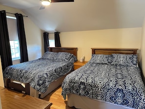 A room with two beds, each with a patterned bedspread, wooden headboards, and a bedside table with a tissue box.