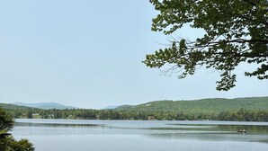Um lago tranquilo com uma área gramada em primeiro plano e uma colina arborizada ao fundo.
