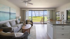 Una sala de estar moderna con un sofá, sillones, una mesa de centro y vista a un césped verde a través de ventanas amplias.
