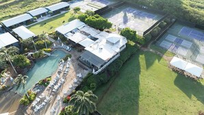 Vista aérea de un resort con piscina, canchas de tenis y restaurante.