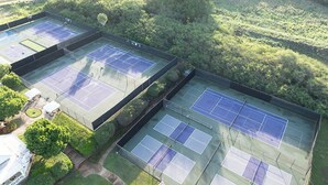 Vista aérea de un complejo de canchas de tenis con varias canchas, rodeado de exuberante vegetación y árboles.