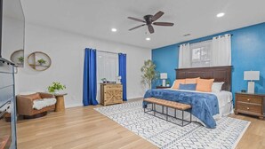 Un dormitorio con cama, banca, mesita de noche, cómoda, silla y ventilador de techo.