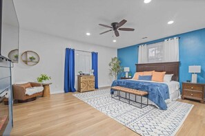 A bedroom with a bed, a bench, a nightstand, a dresser, a chair, and a ceiling fan.