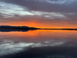 En rolig sø der spejler en solnedgang med bjerge i baggrunden.