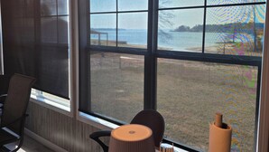 Une pièce dotée d’une grande fenêtre donnant sur une plage, d’un bureau avec une lampe et d’une chaise.