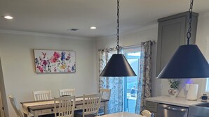 Une cuisine moderne dotée d’un grand îlot central, de planchers en bois foncé, de meubles blancs et d’un luminaire suspendu.